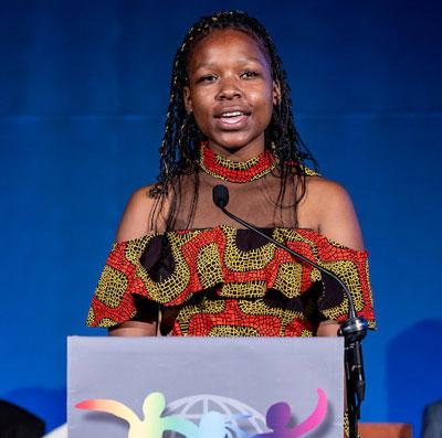Black girl with braids and Zimbabwean dress at podium. 