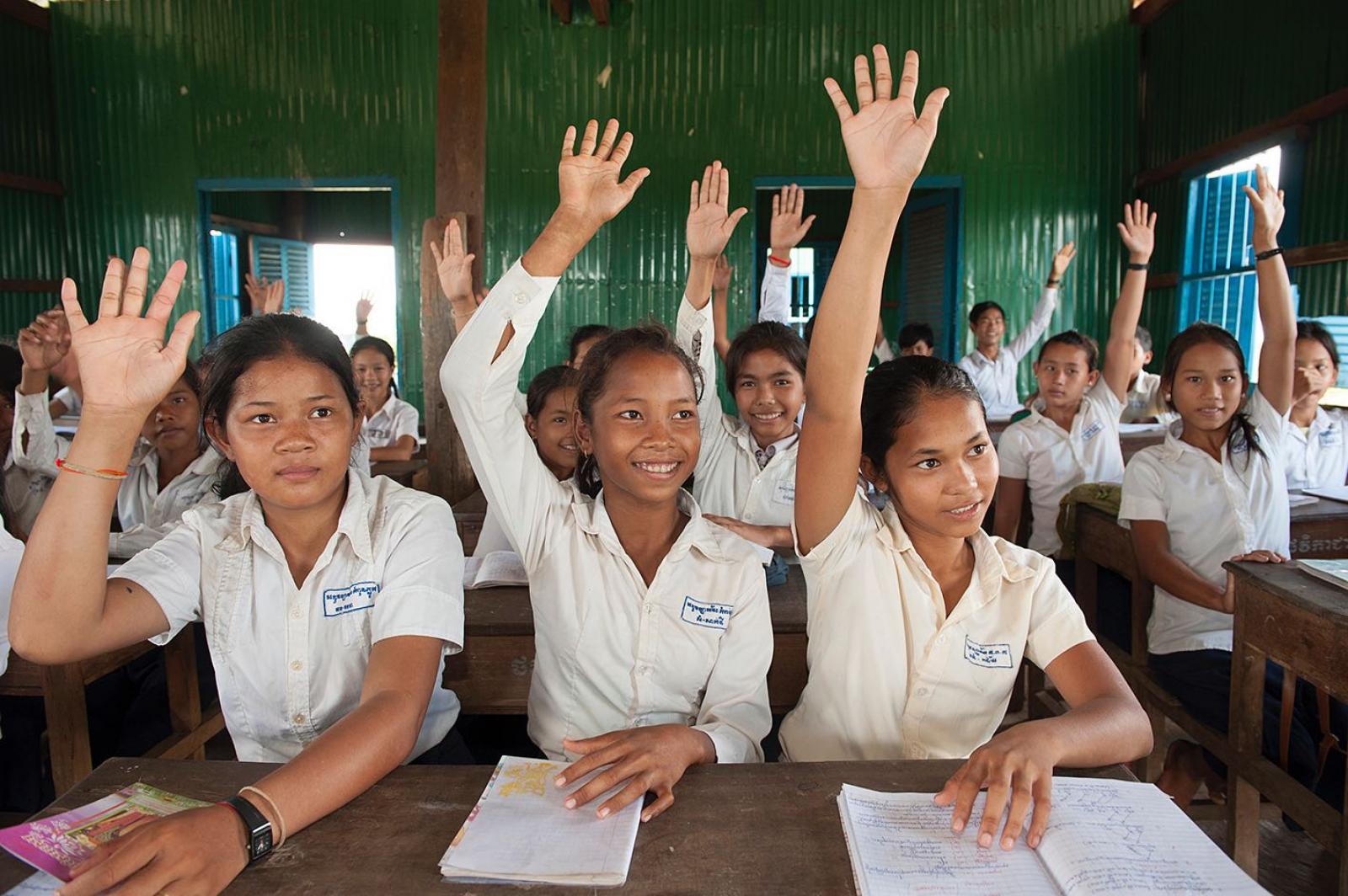 Three girls raising hands in classroom,