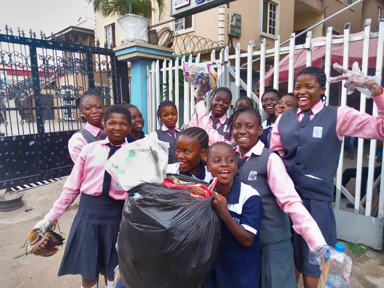 A group of girls smiling, looking into the camera, while holding a big plastic bag of litter