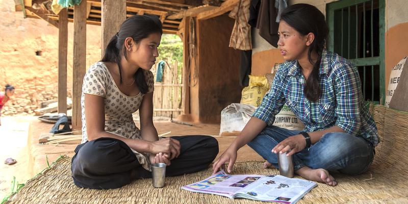 Two girls sitting outside house, discussing