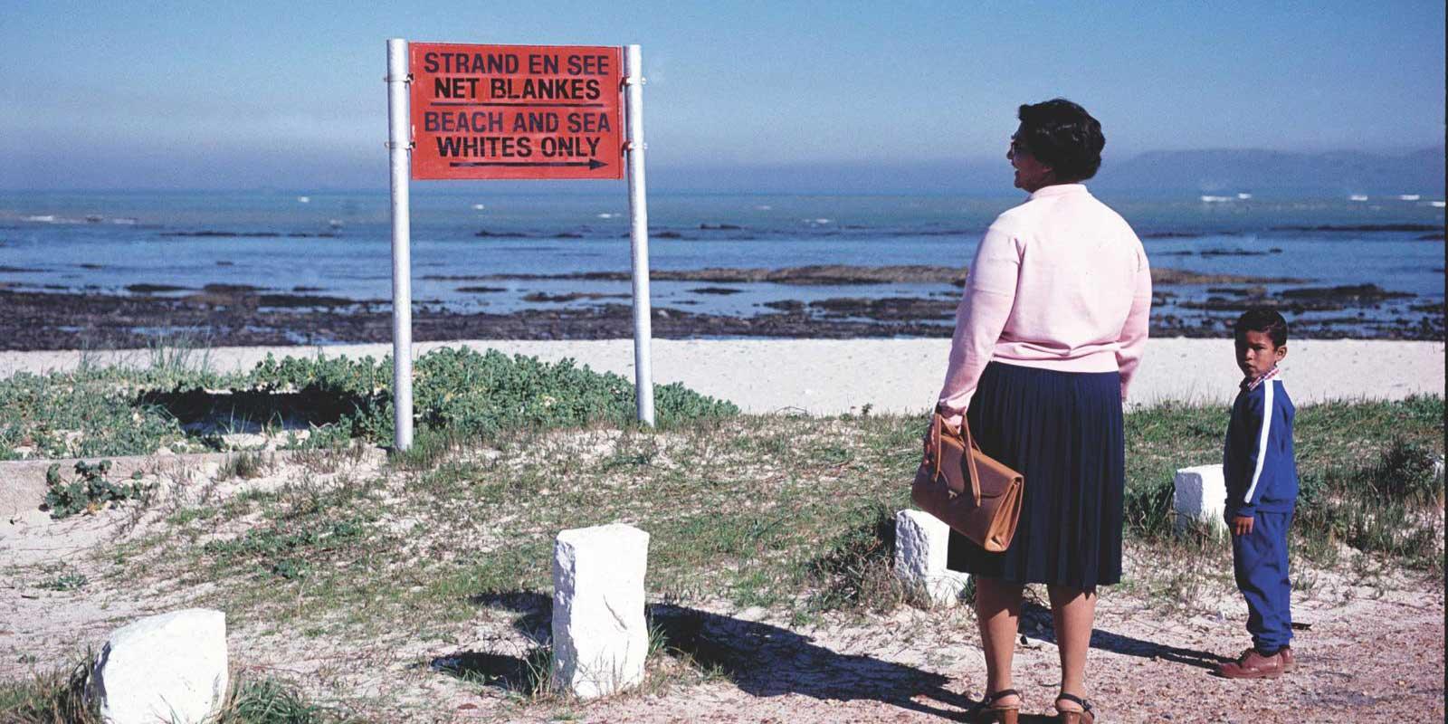 Woman and child look at sign saying Whites only on beach