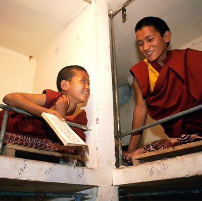 Two boys in monk robes talk and laugh on bunk beds.