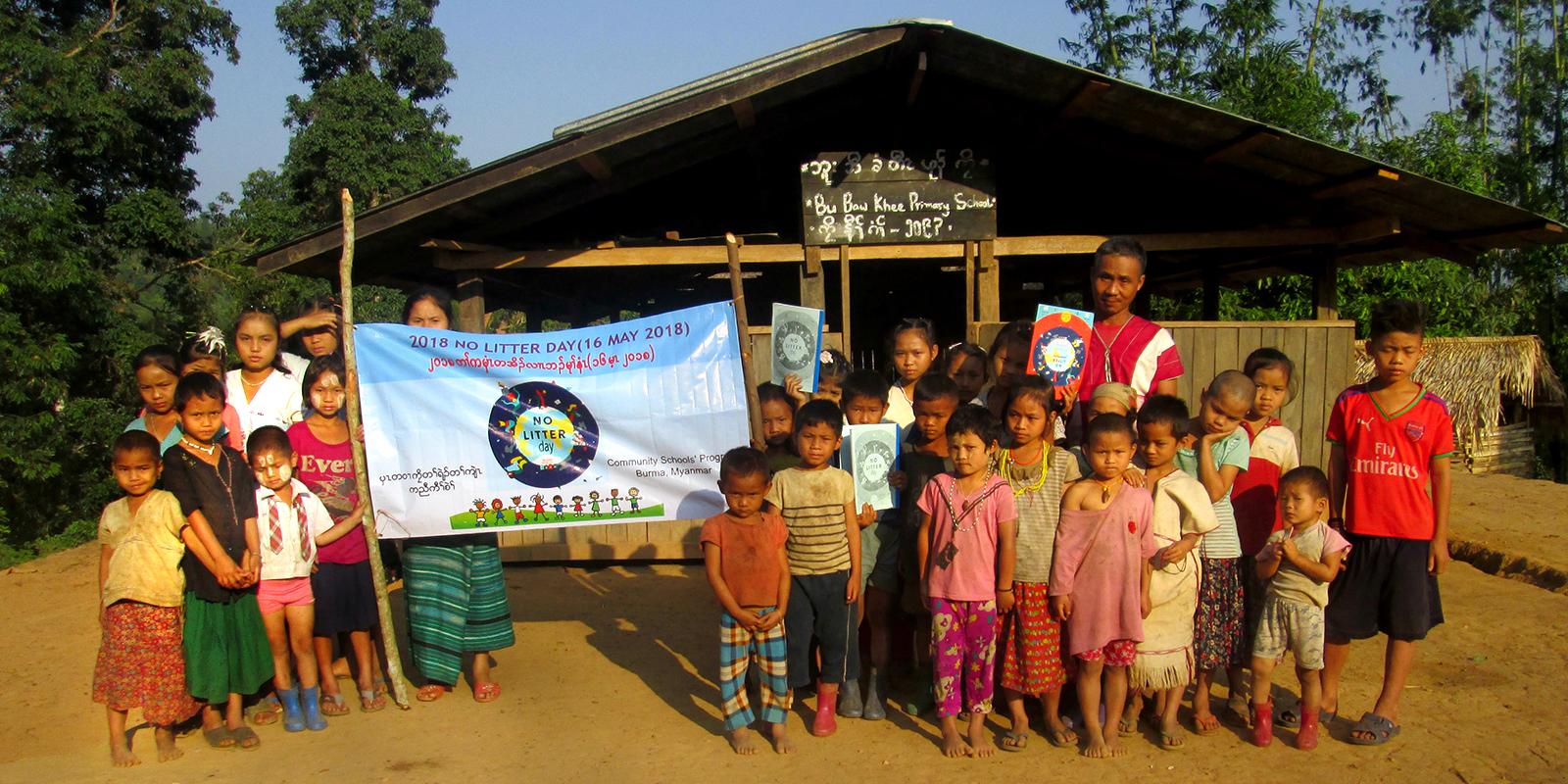 Children standing in front of a house, holding a banner