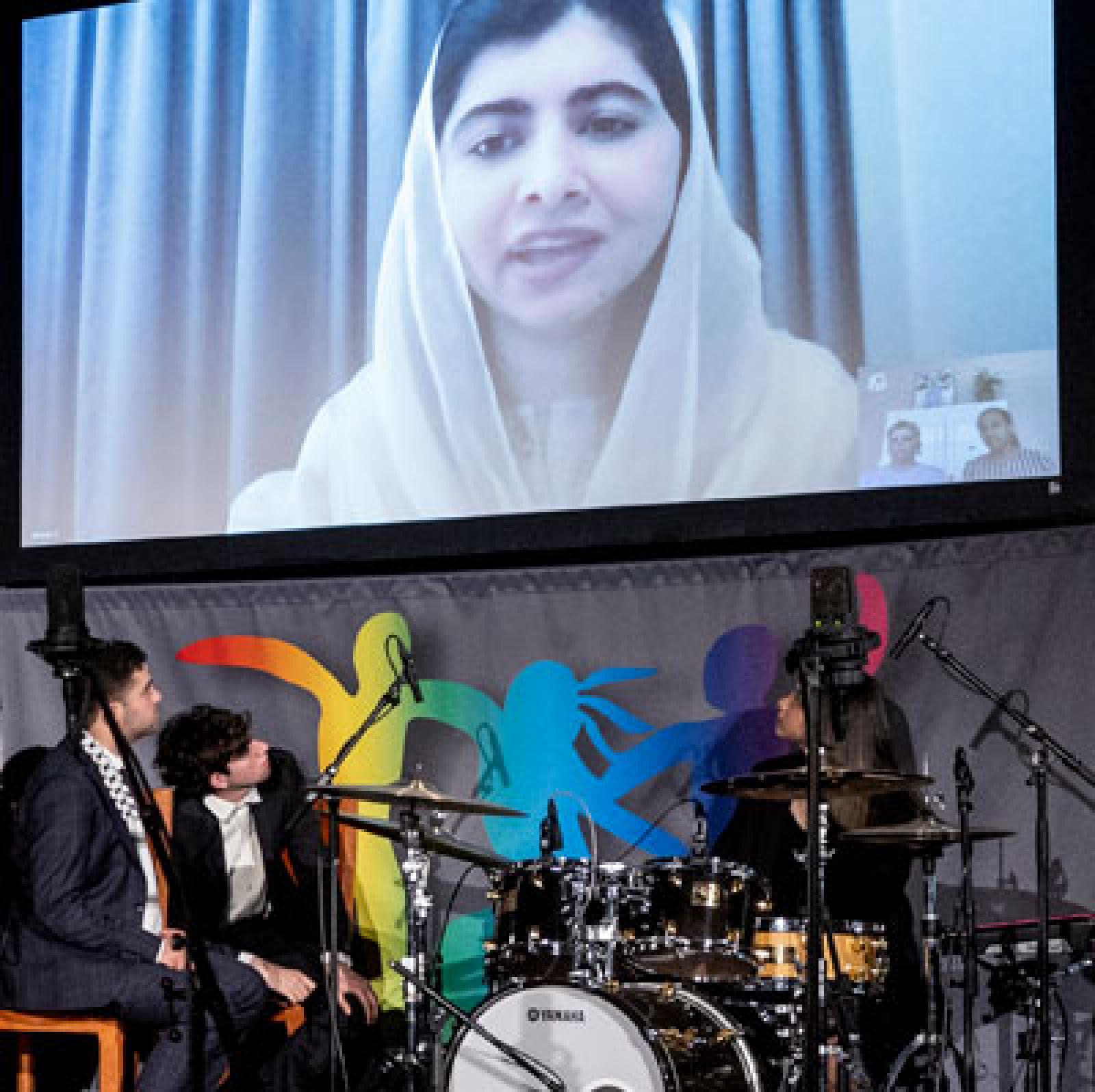 Malala giving speech on large video screen.