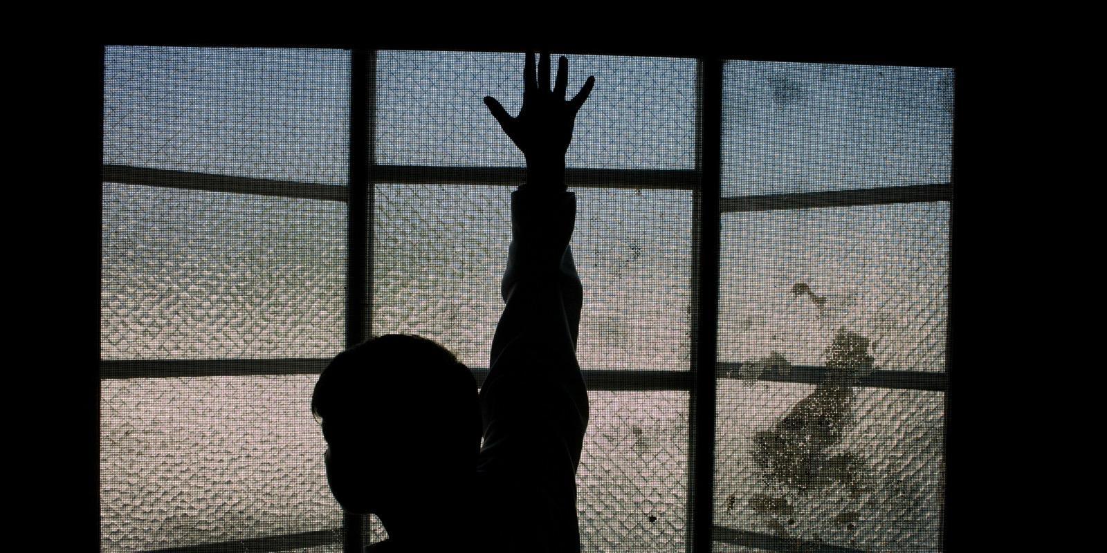 Silhouette of boy against barred window. 