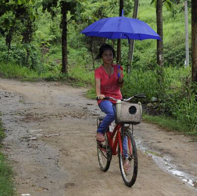 Girl riding a bike on muddy road in green landscape.