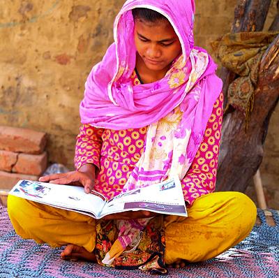 Girl in Pakistan with colorful clothing reading magazine.