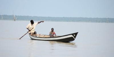 Boy working in boat with big man, on water. 