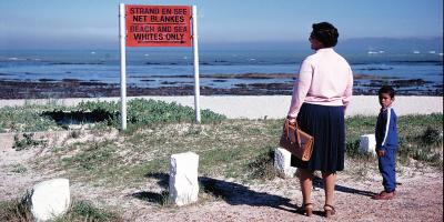 Black lady and child standing on the beach in front of apartheid sign 
