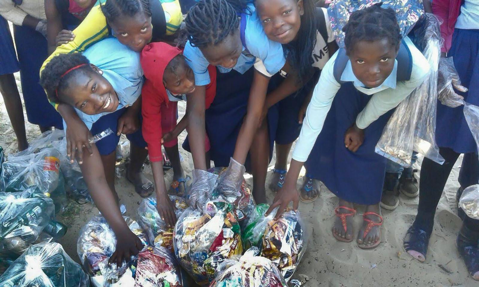 Children looking up into the camera, reaching for plastic bags with litter