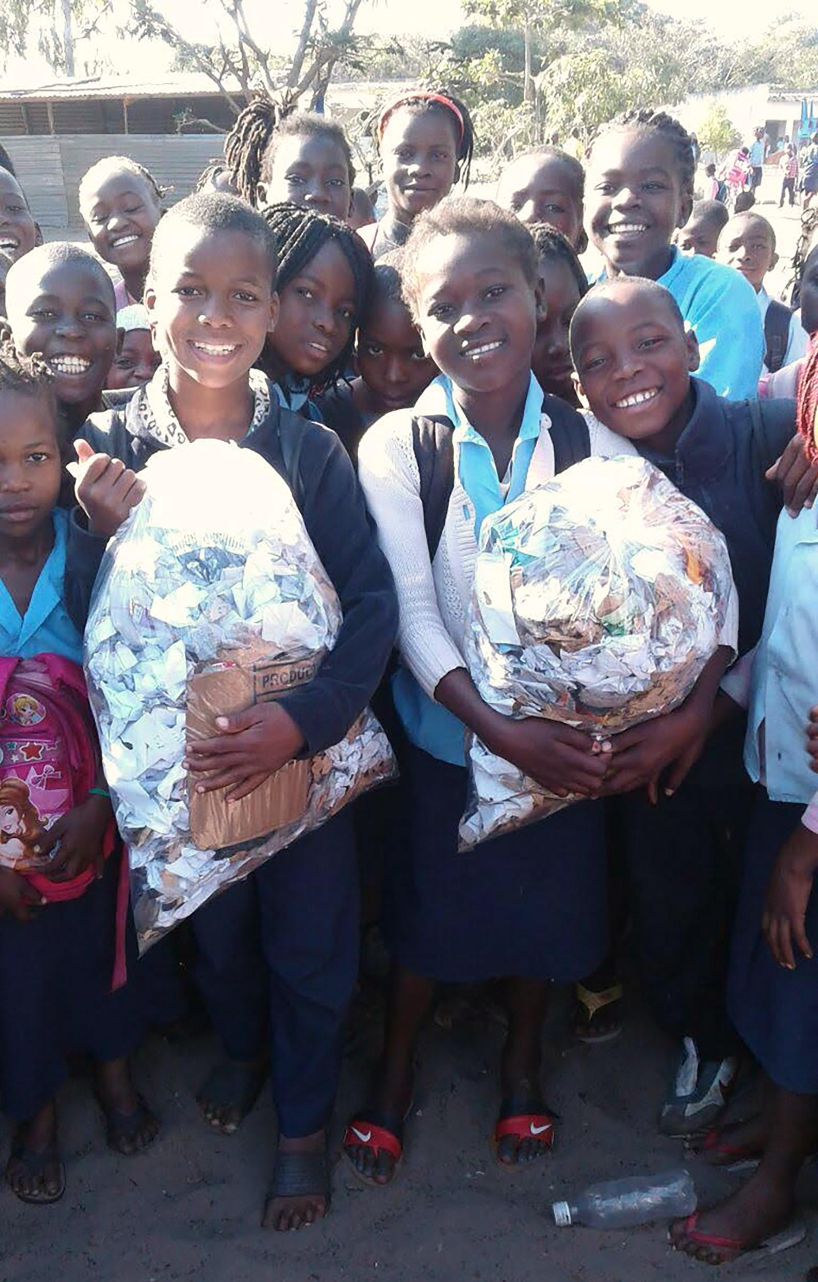Children gathered, smiling into the camera, carrying plastic bags with litter. 