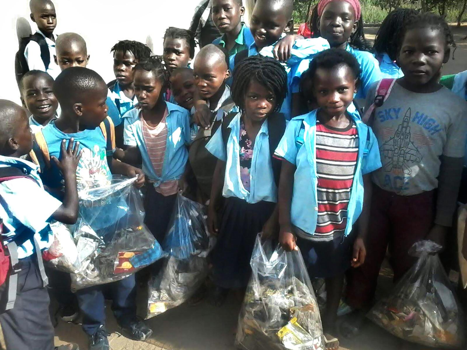 Children dressed in blue open shirts looking into the camera, holding trash bags