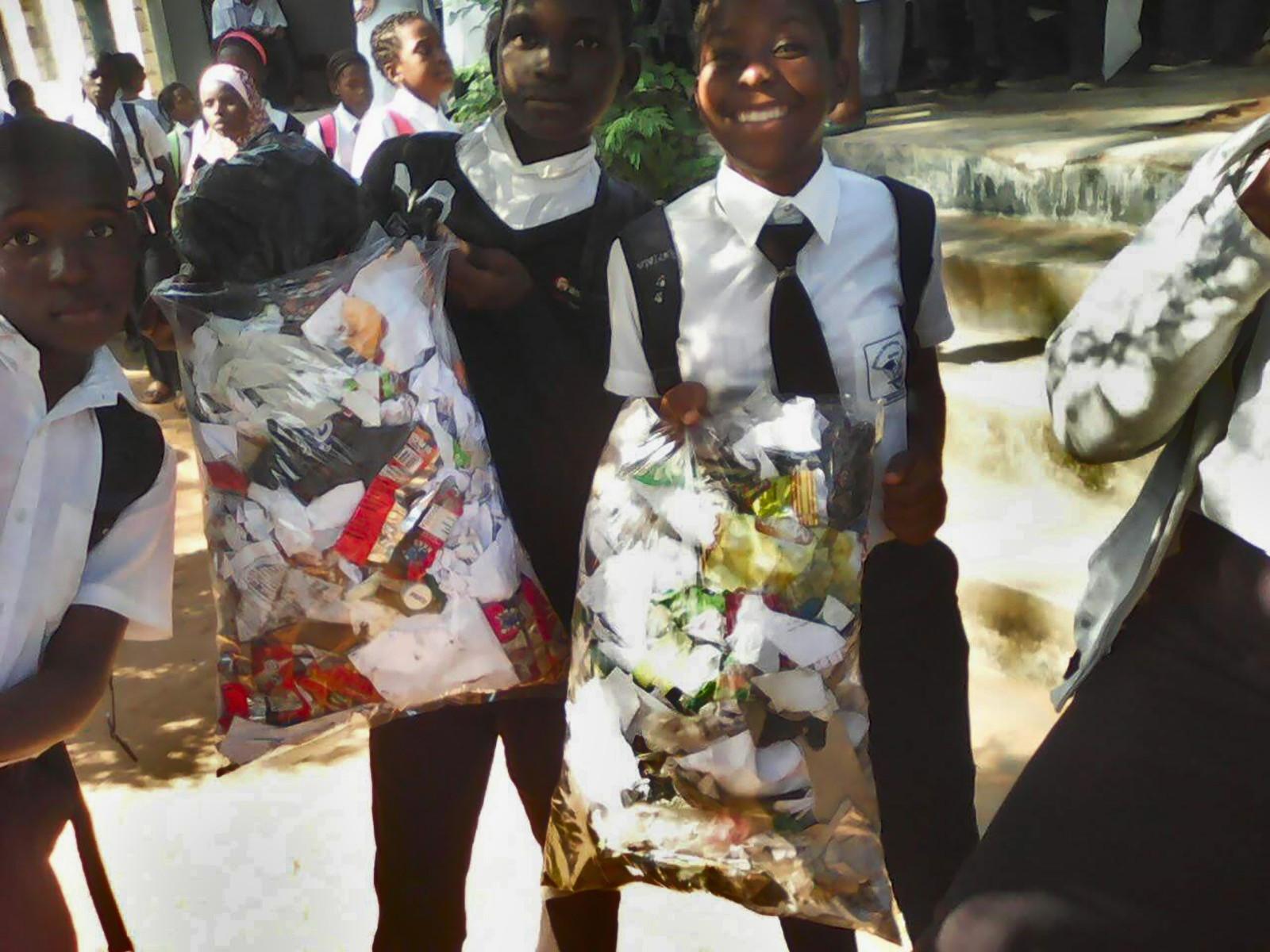 Children dressed in white shirts and tie, holding trash bags