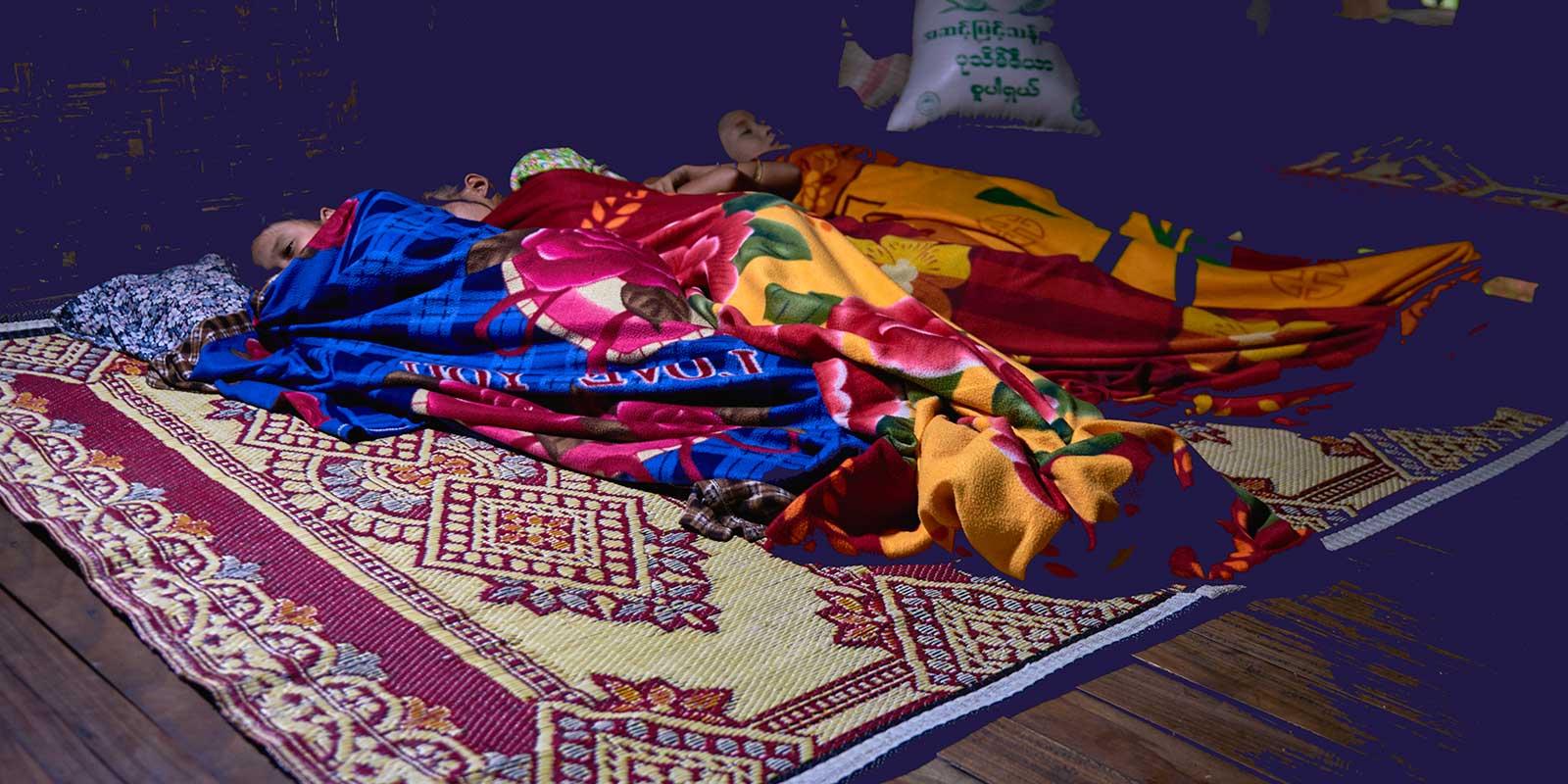 Children sleeping on floor under colourful blankets.