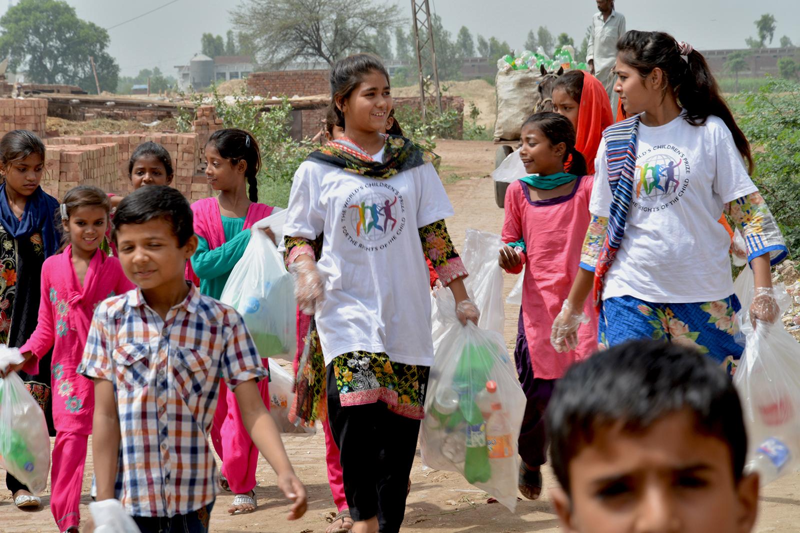 Children in different ages walking together, carrying plastic bags with litter 