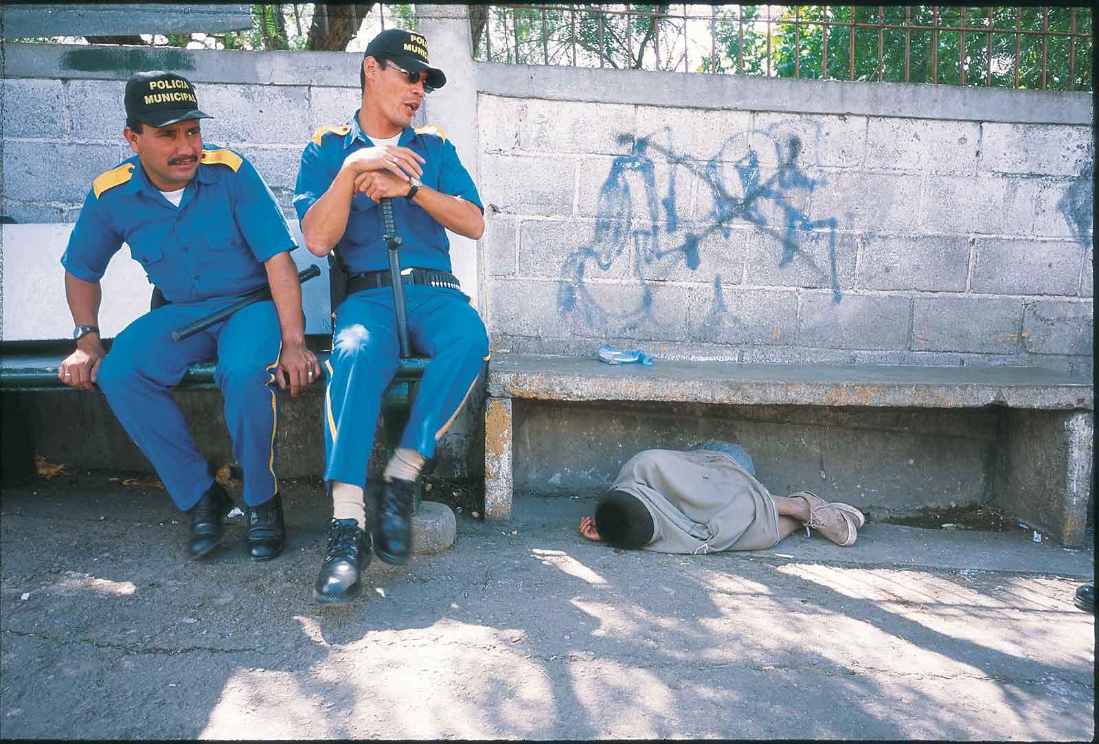 Child sleeping under bench, two police men watching.