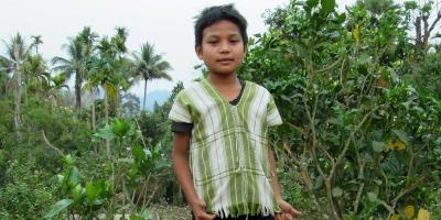 Small boy standing in green forest wearing striped shirt.