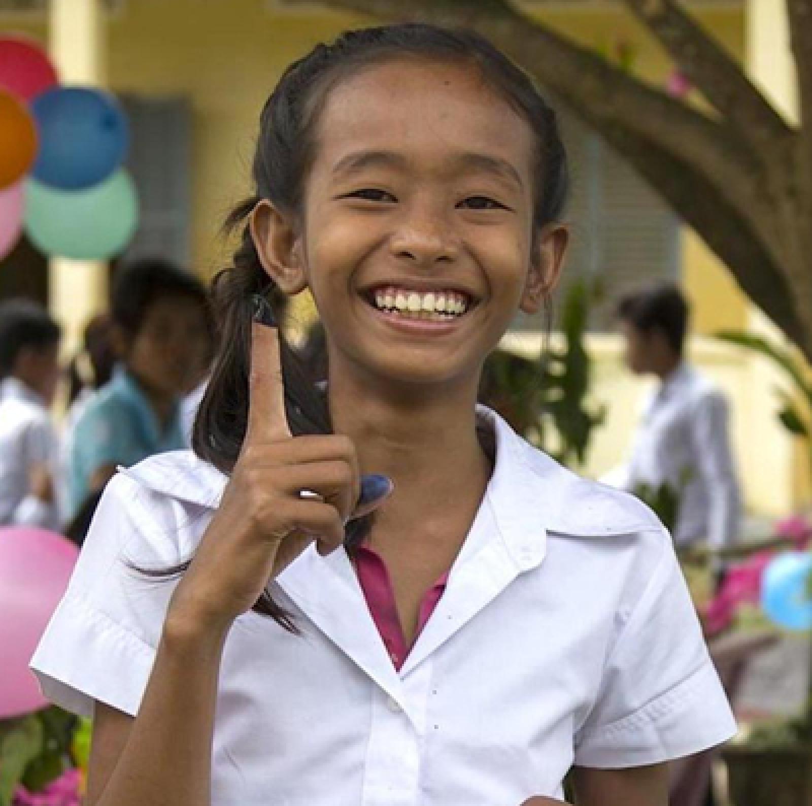 Girl holding up finger, smiling.