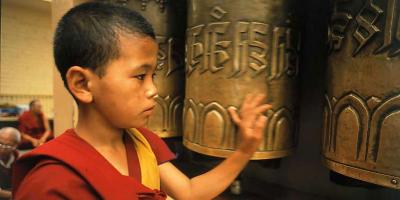 Boy in monk robe spinning brass prayer wheels in temple. 
